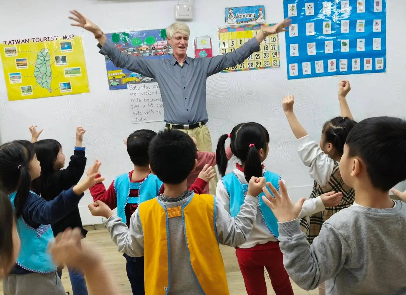 外師張開雙臂帶動課堂，孩子們興奮舉手