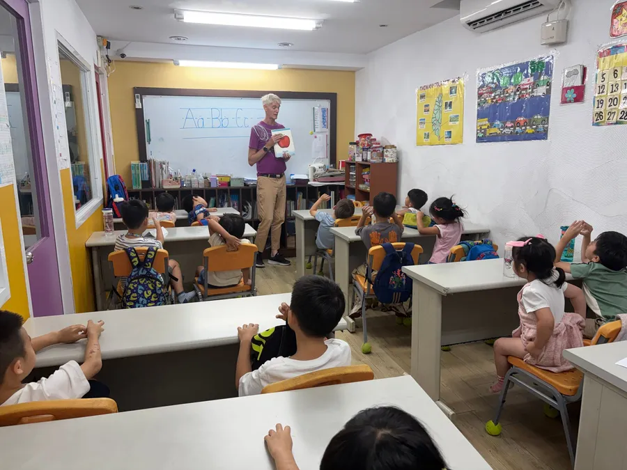 老師在白板前展示蘋果圖卡，學生坐在座位上看著前方
